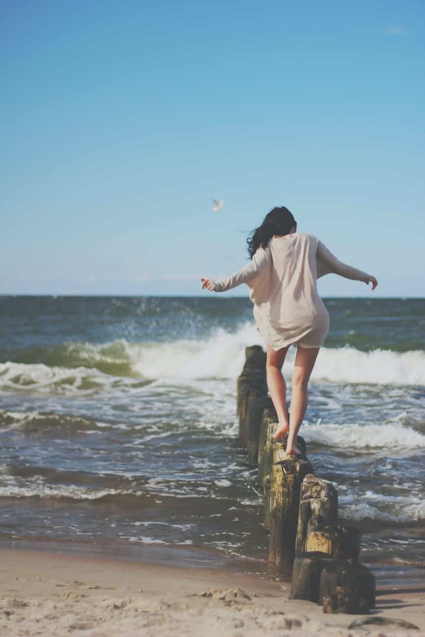 woman wearing brown long sleeved dress stepping on brown pillar stands